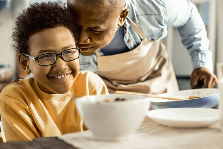 Family PDA. Cute curly boy squinting at how his pleasant father leaning on him with love.の写真素材