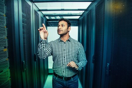 Futuristic technology. Nice handsome man standing in front of the transparent screen while looking at itの写真素材
