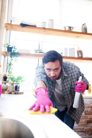 Man using detergent. Dark-haired man wearing gloves using detergent while cleaning tableの写真素材
