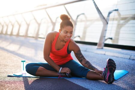 Stretching legs. Dark-haired young woman with hair bun stretching legs while doing yoga