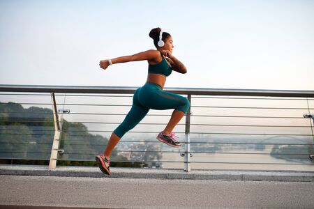 Running fast. Dark-skinned woman wearing white earphones running fast while enjoying training