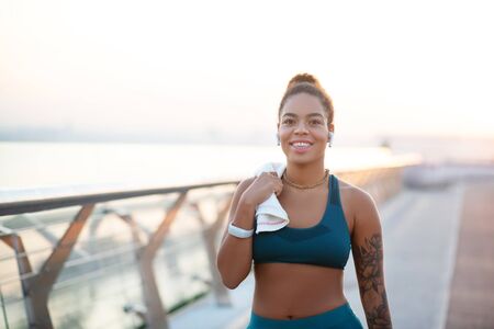 Woman holding towel. Beaming dark-eyed woman holding towel while walking after intensive run