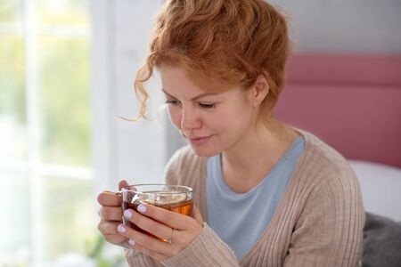 Drinking tea. Curly sick woman feeling good while drinking hot tea and having positive thoughts