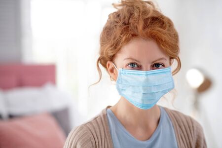 Woman in mask. Young blue-eyed woman wearing mask while having flu and feeling terribleの写真素材