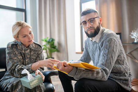 Helping servicewoman. Bearded psychoanalyst wearing glasses helping servicewoman with anxiety