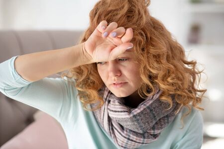 Having fever. Red-haired woman touching her forehead while having fever after catching cold