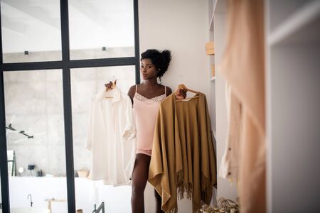 Woman holding hangers. Slim appealing woman holding hangers with clothing while choosing outfitの写真素材