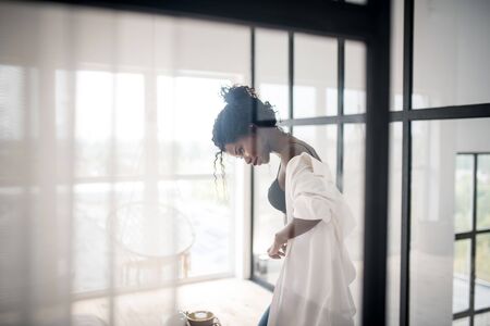 Standing near table. Curly dark-skinned woman dressing up standing near table in the kitchenの写真素材
