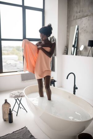Woman in towel. Slim appealing dark-skinned woman taking towel after chilling in bathの写真素材