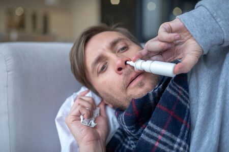 Having stuffy nose. Blue-eyed man having stuffy nose and headache taking nasal sprayの写真素材