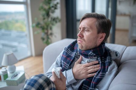 Coughing all day. Man wearing checked scarf coughing all day long while having fluの写真素材