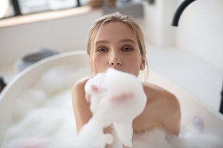 Foam in hands. Blue-eyed cheerful woman holding foam in her hands while having bathの写真素材