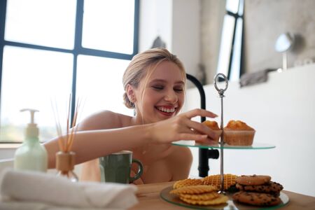 Woman taking cupcake. Smiling woman taking cupcake in the morning while sitting in bathの写真素材