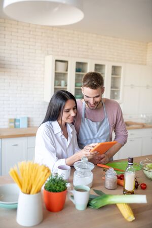 Showing culinary recipe. Dark-haired beaming wife showing culinary recipe to her husbandの写真素材