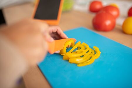 Girl slicing pepper. Close up of girl slicing up yellow bell pepper while cooking breakfastの写真素材