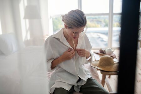 Putting shirt on. Young stylish blonde woman putting shirt on while preparing for workの写真素材