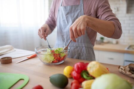 Salad in bowl. Close up of young man mixing salad with lettuce and pepper in bowlの写真素材