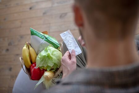 Receipt in hands. Close up of receipt in hands of man after doing groceries shoppingの写真素材