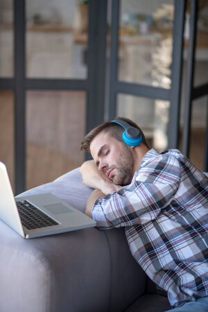 Having a nap. Bearded man wearing checked shirt having a nap after working on his laptop