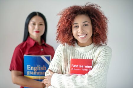Holding Chinese book. Curly red-haired woman holding Chinese book while standing near friendの写真素材