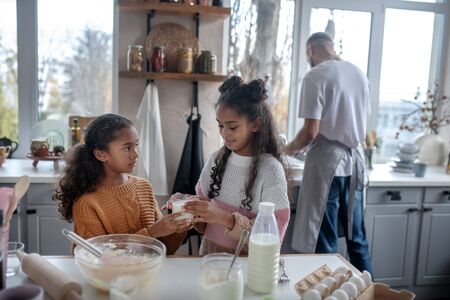 Glass of milk. Cute daughters taking glass of milk while cooking pie with fatherの写真素材