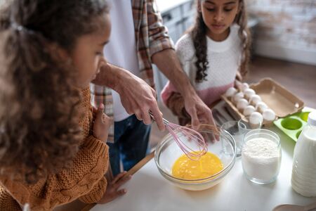 Girls watching father. Girls watching their father whipping eggs while cooking pie at the weekendの写真素材
