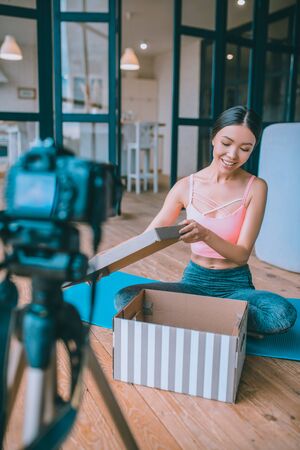 Opening box. Fitness blogger smiling while opening box with present from follower and filming video