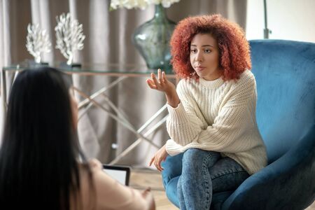 Speaking with psychologist. Young woman wearing jeans and sweater speaking with psychologistの写真素材