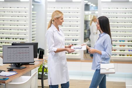 Buying new glasses. Dark-haired stylish woman smiling while buying new nice glasses in optical storeの写真素材