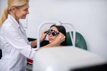 Eye doctor smiling. Blonde-haired experienced eye doctor smiling while examining pleasant patientの写真素材