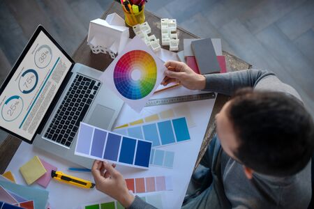 Color for project. Top view of interior designer choosing color for project while sitting near laptopの写真素材