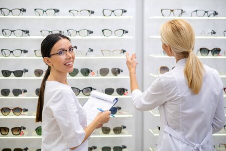 Helping doctor. Dark-eyed assistant of ophthalmologist helping experienced eye doctor in medical storeの写真素材