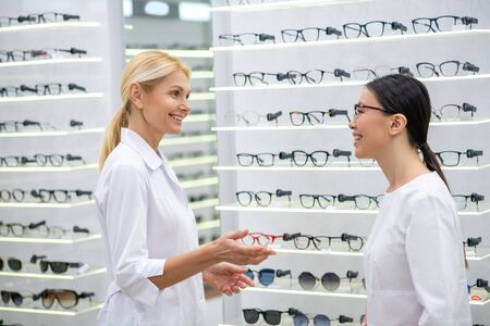 Greeting new assistant. Eye doctor smiling broadly while greeting her new assistant in the optical storeの写真素材