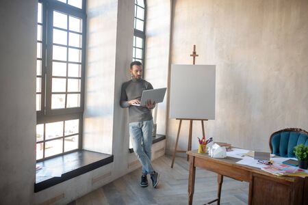 Designer holding laptop. Interior designer holding laptop while standing near window in spacious roomの写真素材