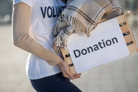 Donation time. Close up of volunteer wearing jeans and white t-shirt caring box with donationの写真素材