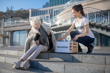Bringing donation. Volunteer bringing donation for poor homeless woman spending day outside