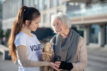 Supporting poor woman. Kind-hearted volunteer supporting poor woman while bringing bread and teaの写真素材