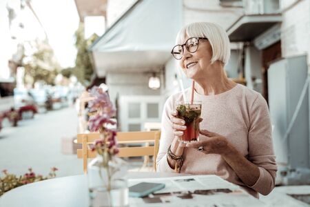 Tasty drink. Positive aged woman sitting at the table while enjoying her tasty cocktailの写真素材