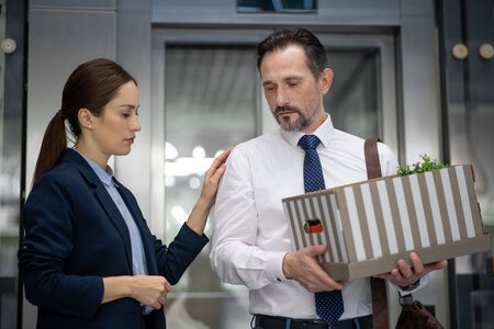 Supporting friend. Dark-haired colleague supporting her bearded mature friend from office after...