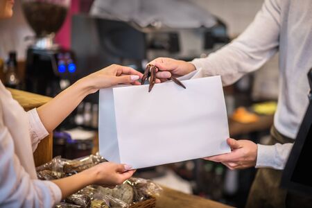 Bag with order. Close up of cashier passing bag with order to the customer in the morning