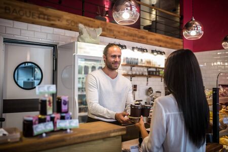 Coffees for customer. Handsome barista giving two takeaway coffees to the customer in the morningの写真素材