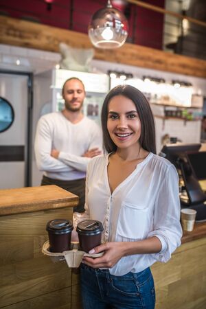 Woman holding coffee. Dark-haired businesswoman wearing white blouse holding two takeaway coffeesの写真素材