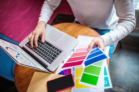 Choosing color. Clos up of interior designer choosing color while working hard using laptop and phoneの写真素材