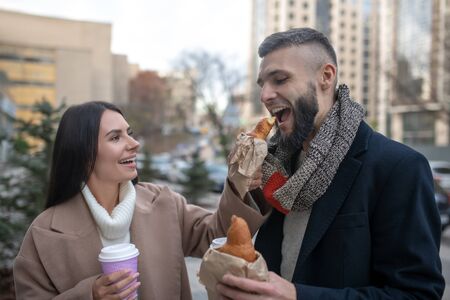 So tasty. Hungry young man biting a delicious croissant while being fed by his wifeの写真素材
