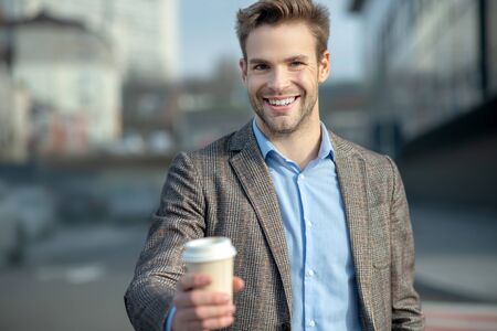 Beautiful smile. Young handsome man in a jacket smiling positively holding a cup of coffee