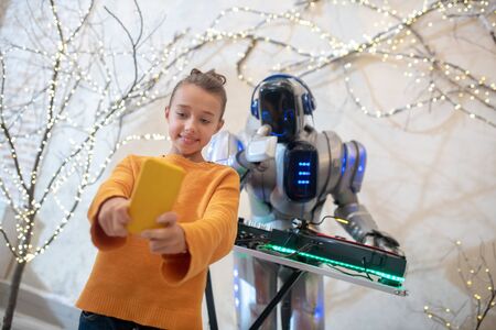 Selfie. Cute girl making a selfie with robot dj standing near dj table