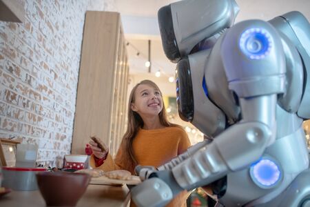 Admiration. Pretty beaming girl looking at house robot with admiration and smiling