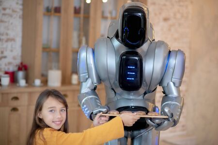 Robotic cooker. Cute blue-eyed girl demonstrating meat balls made by house robot feeling proudの写真素材