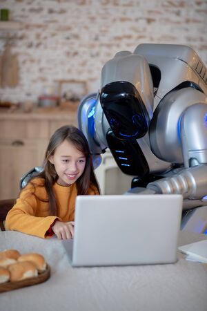 Interesting task. Robot and a girl in orange shirt looking involved while doing homework togetherの写真素材