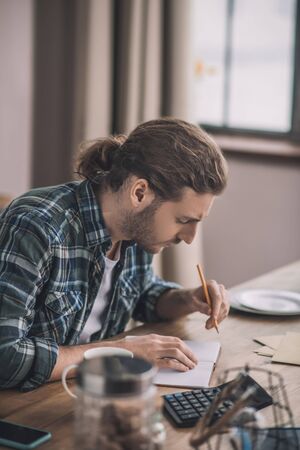 Handwriting. Young long-haired man writing on the piece of paperの写真素材